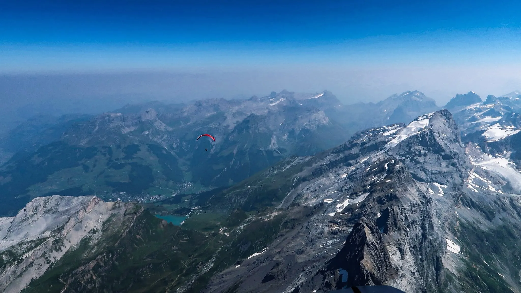 Weiter Blick über ein Tal: ein einzelner roter Gleitschirm auf dem Weg zur nächsten Bergkette.